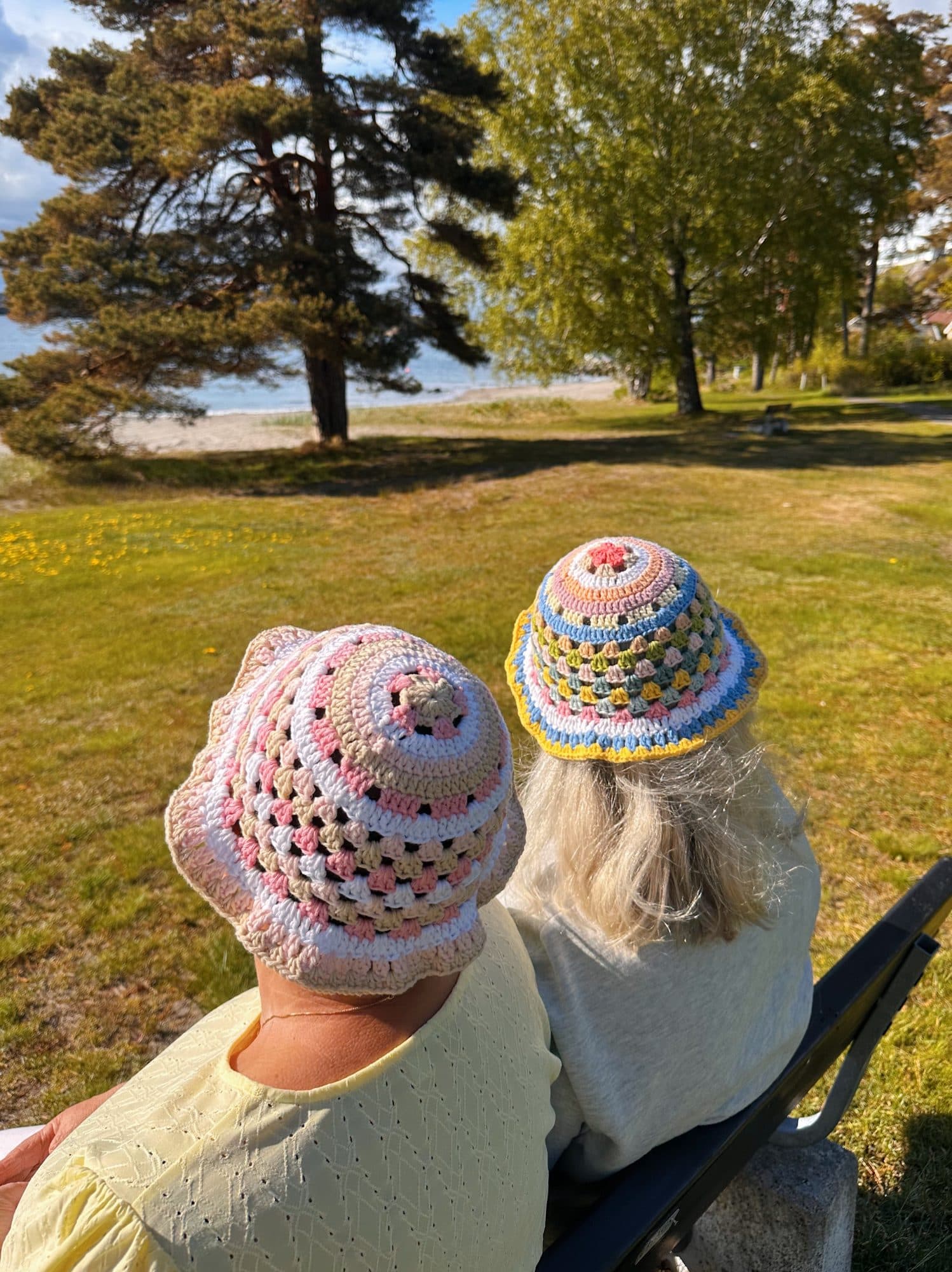 To personer med fargerike heklede bøttehatter på benk ved stranden